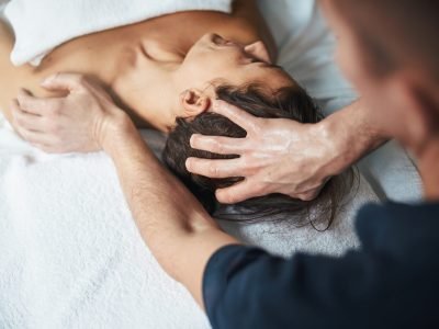Close up back view portrait of brunette female lying on massage bed while massage therapist doing relax therapy on her head in wellness clinic