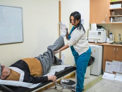 Nurse performing rehabilitation exercise on an elderly male patient in a nursing home or healthcare facility, aiding recovery