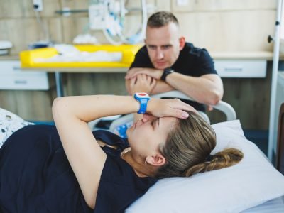 Woman lying feeling pain during childbirth. Pregnancy, childbirth concept. Caring man holding pregnant wife's hand during childbirth. Supportive man helping young woman during childbirth.
